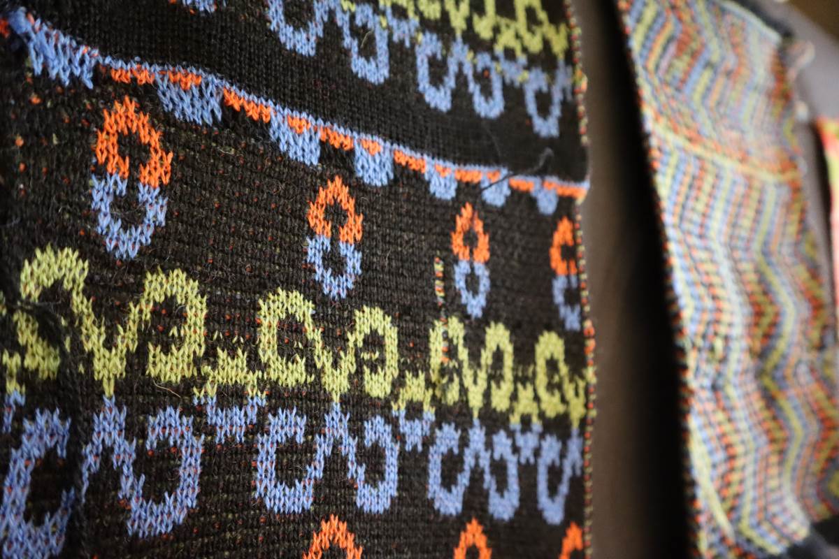 Strikket prøvelapp med sort bunnfarge og blå,grønn og oransje krullemønster